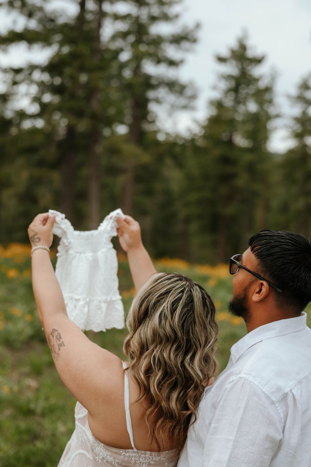 Couple celebrating pregnancy announcement in an outdoor woodland setting.