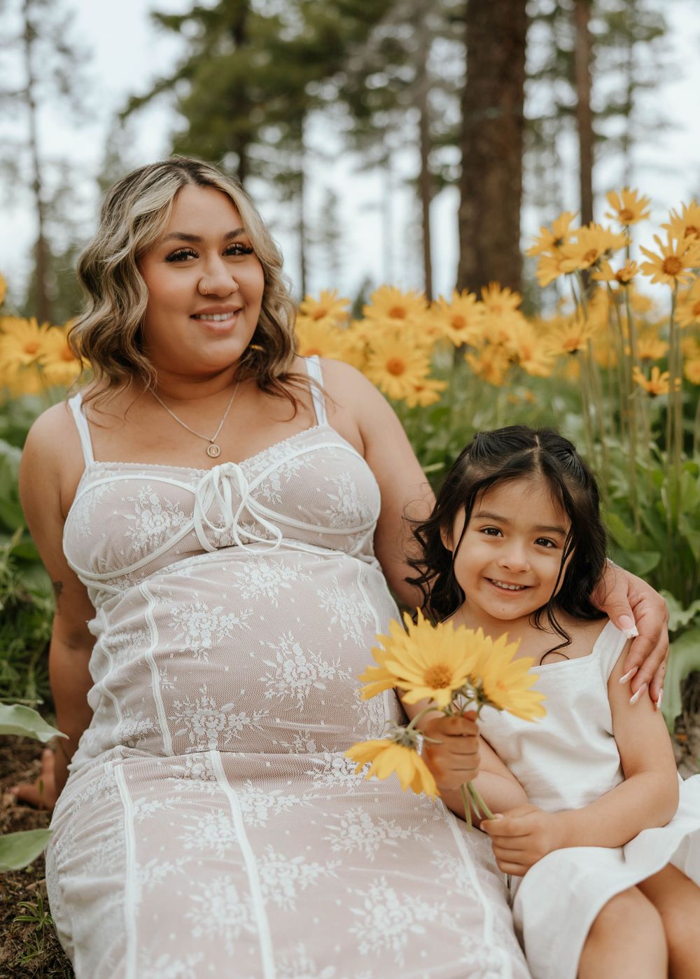 Maternity portrait with child in white dresses surrounded by yellow flowers.