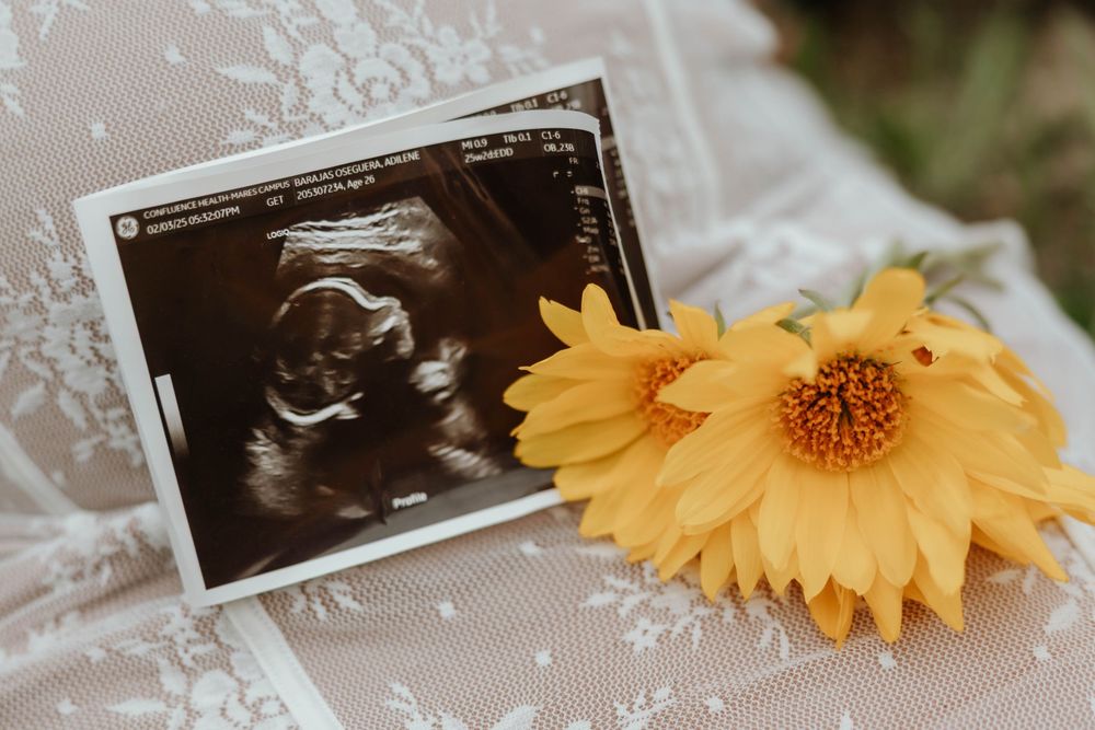Ultrasound photos displayed with yellow daisy flower against white lace fabric.
