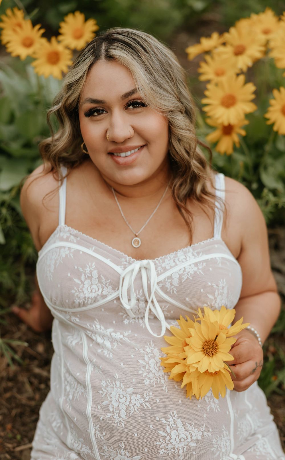Beautiful maternity photos in a sunflower field featuring a white lace dress and golden blooms.