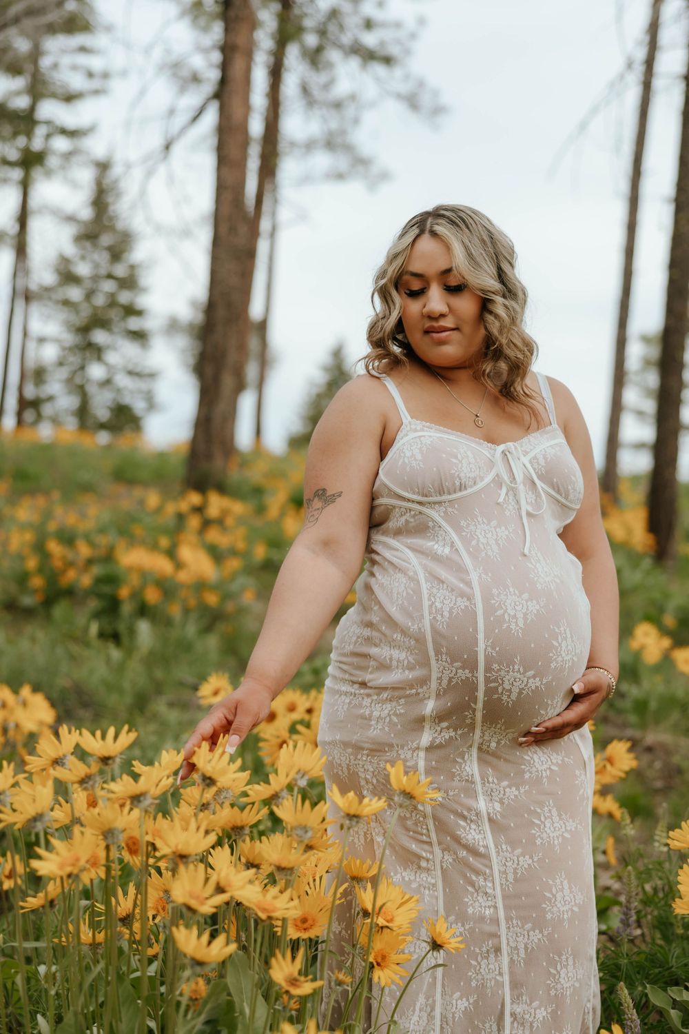 Maternity portraits among vibrant yellow wildflowers in a scenic mountain setting.