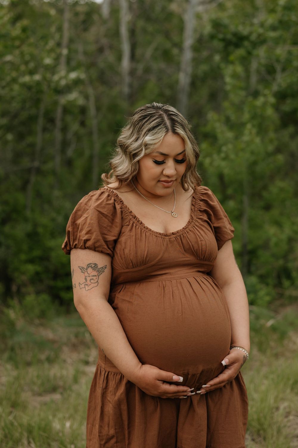 Maternity photos in a brown dress showcasing the baby bump in a natural forest setting.