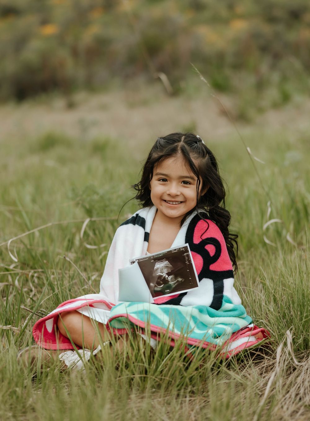 Child lying in grass with colorful blankets during an outdoor photoshoot.