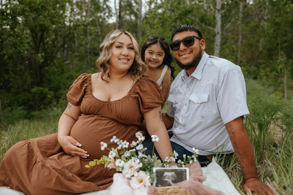 Maternity photo session in a field with yellow wildflowers and pine trees.