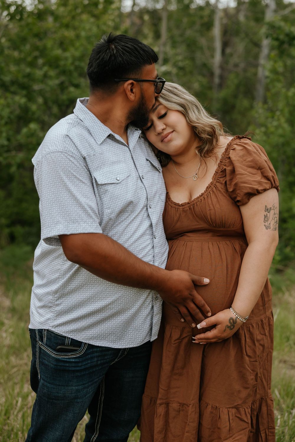 Intimate maternity photos of couple embracing in a wooded setting.