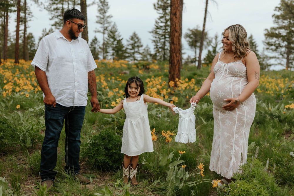 A family walks together through a field of wildflowers with evergreen trees in the background.