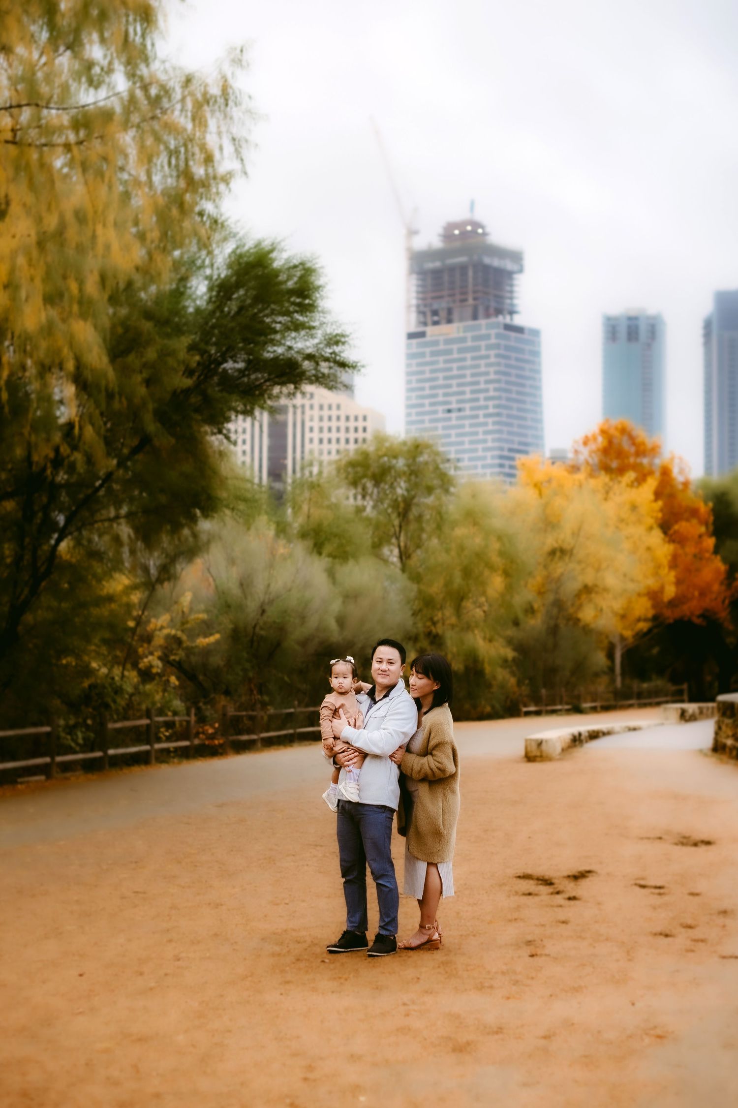 Autumn cityscape with tall buildings in the background and fall foliage framing a sandy path in a park.