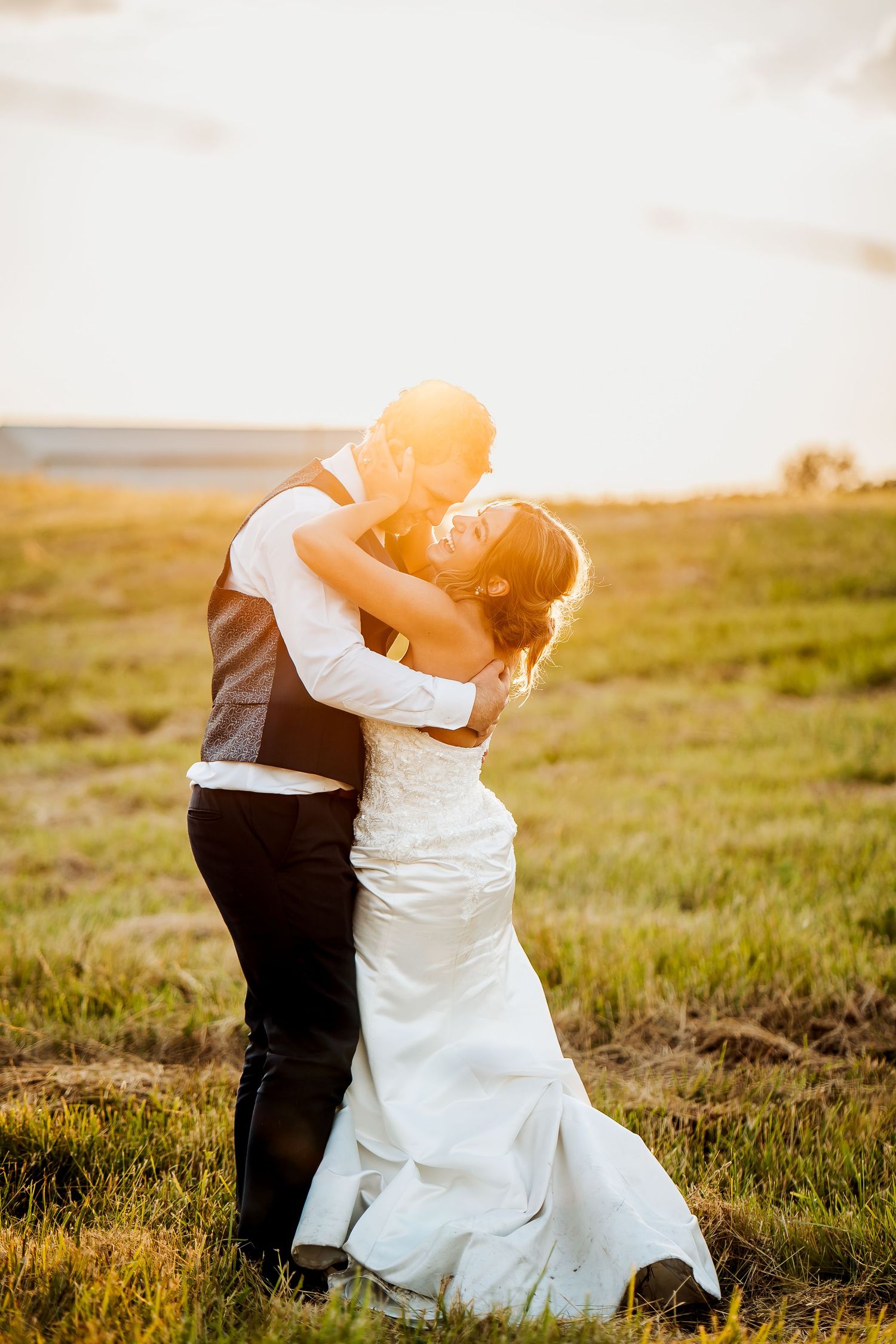 A romantic wedding couple embraces in a sunlit meadow at golden hour with warm rays illuminating their silhouette.