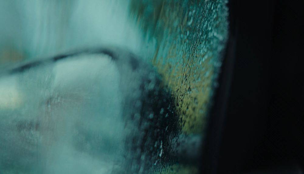 Abstract water droplets on glass creating artistic blur effect in teal tones.