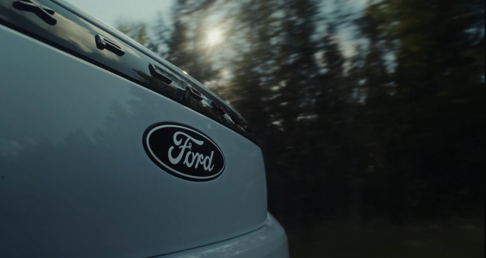 Close-up detail of Ford vehicle emblem with blurred forest background.
