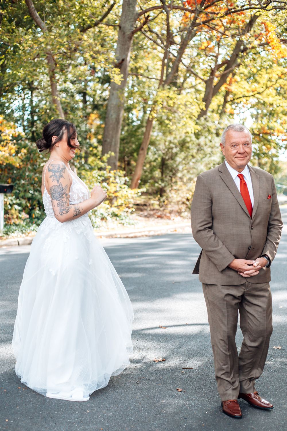 Wedding couple poses for outdoor autumn photos on paved pathway surrounded by fall foliage.