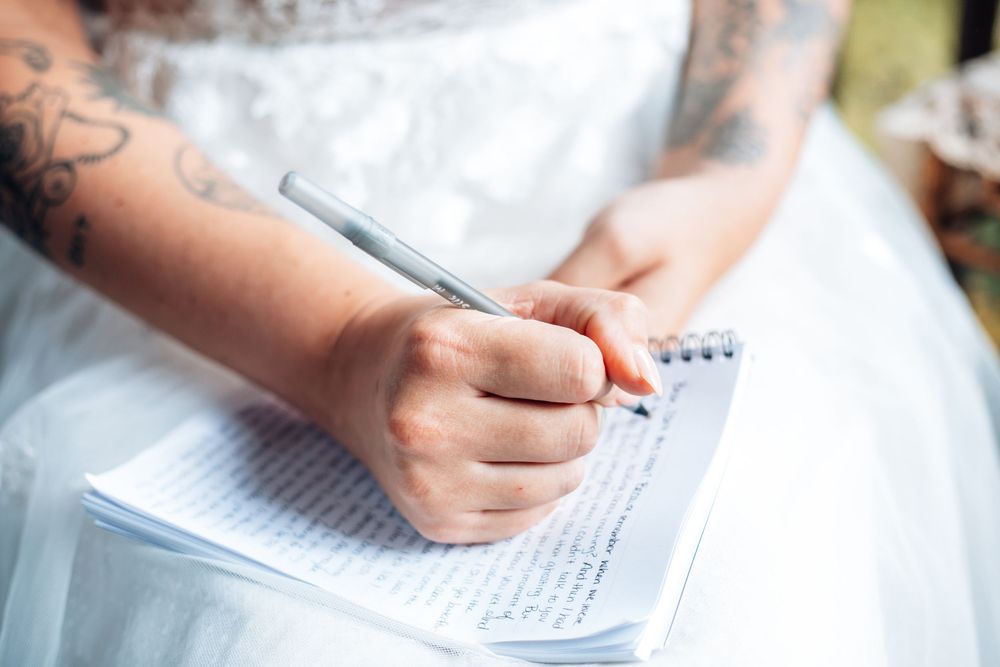Close-up of hands writing personal wedding vows in white dress.