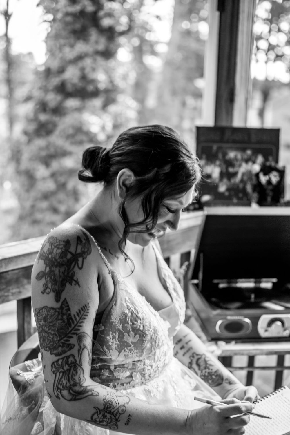 Bride in lace dress with tattoos preparing for wedding day in natural window light.