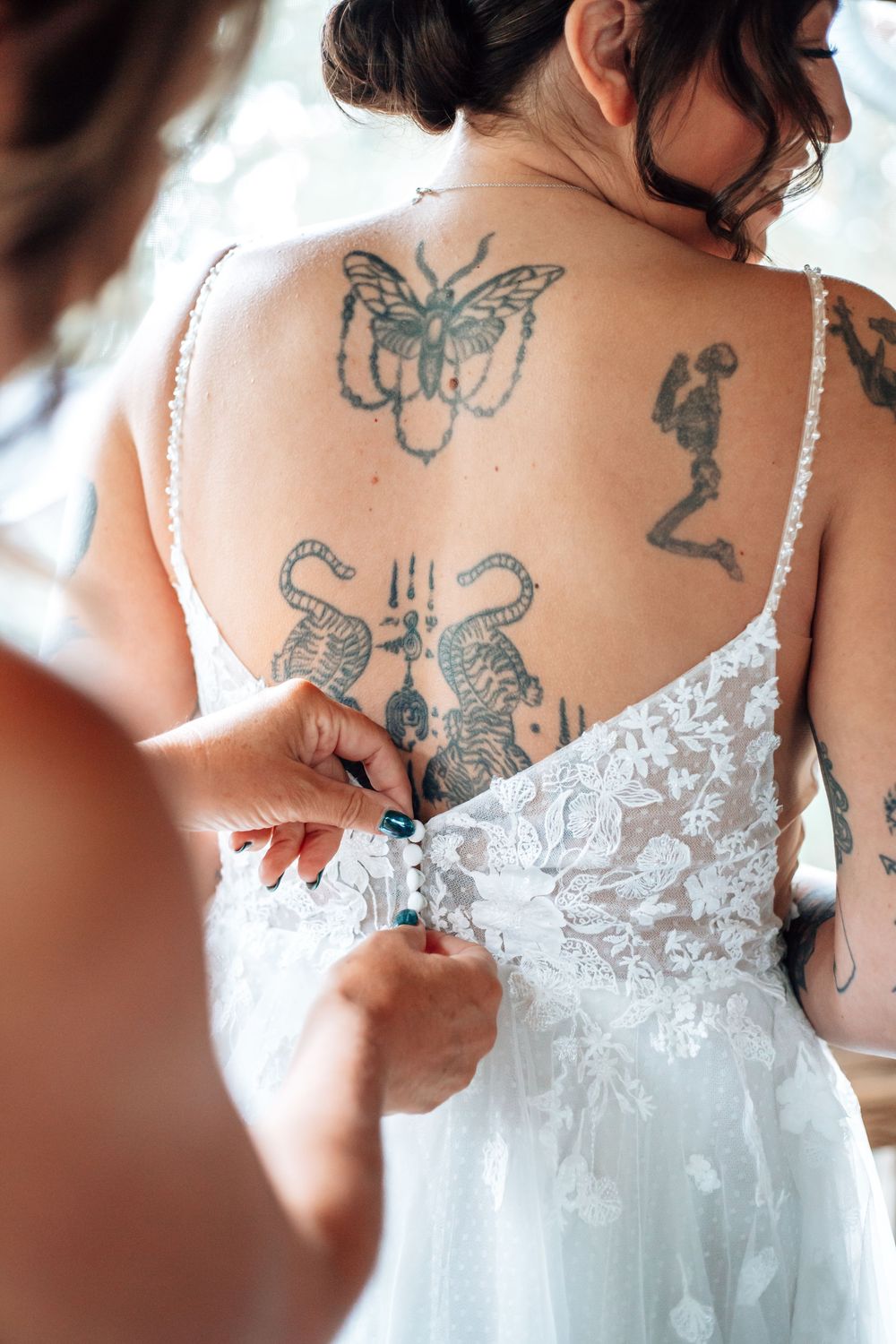 Close-up of intricate lace details and butterfly tattoos on the back of a white wedding dress.