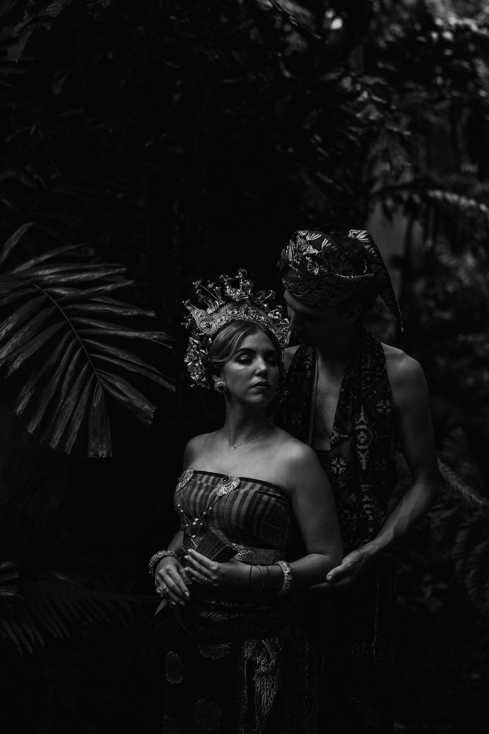 Dramatic black and white portrait in a tropical garden setting with ornate headpieces.