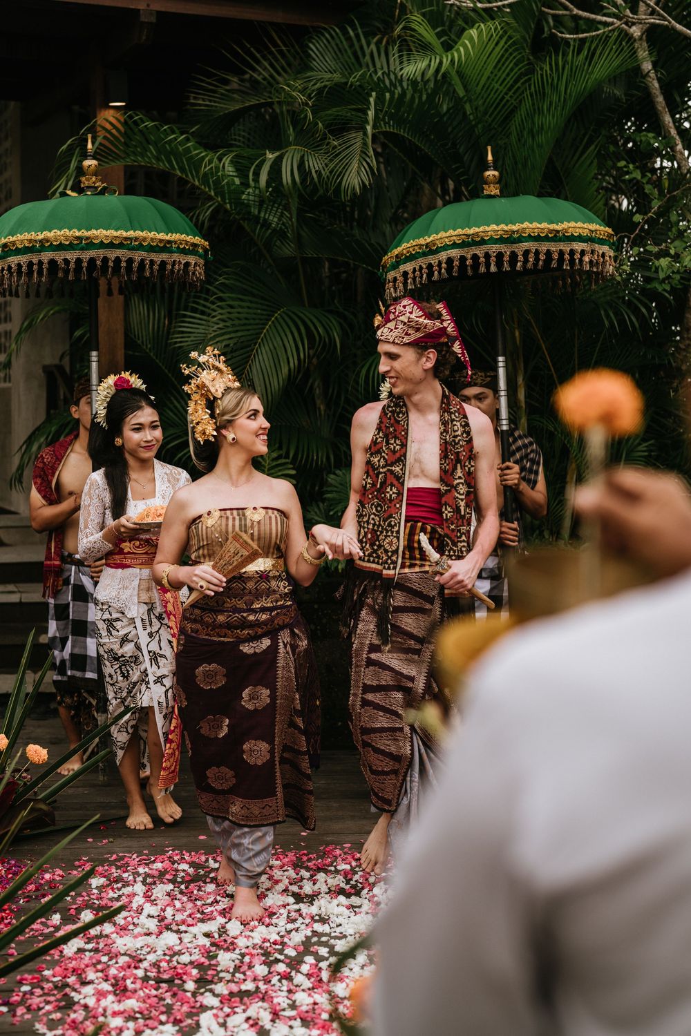 Wedding ceremony with rose petals scattered on the ground under green parasols.