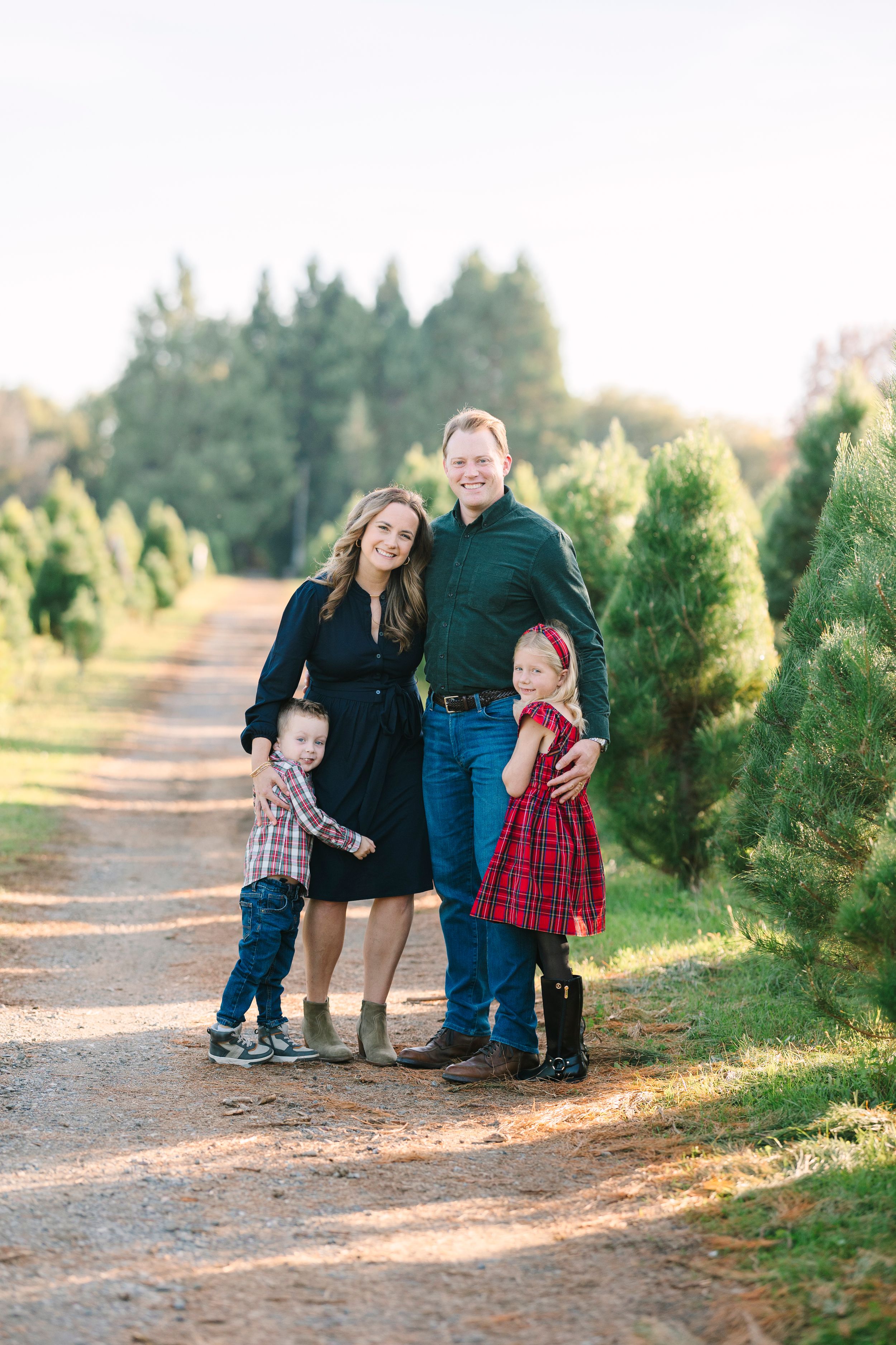 Family group poses casually together among evergreen trees at sunset.