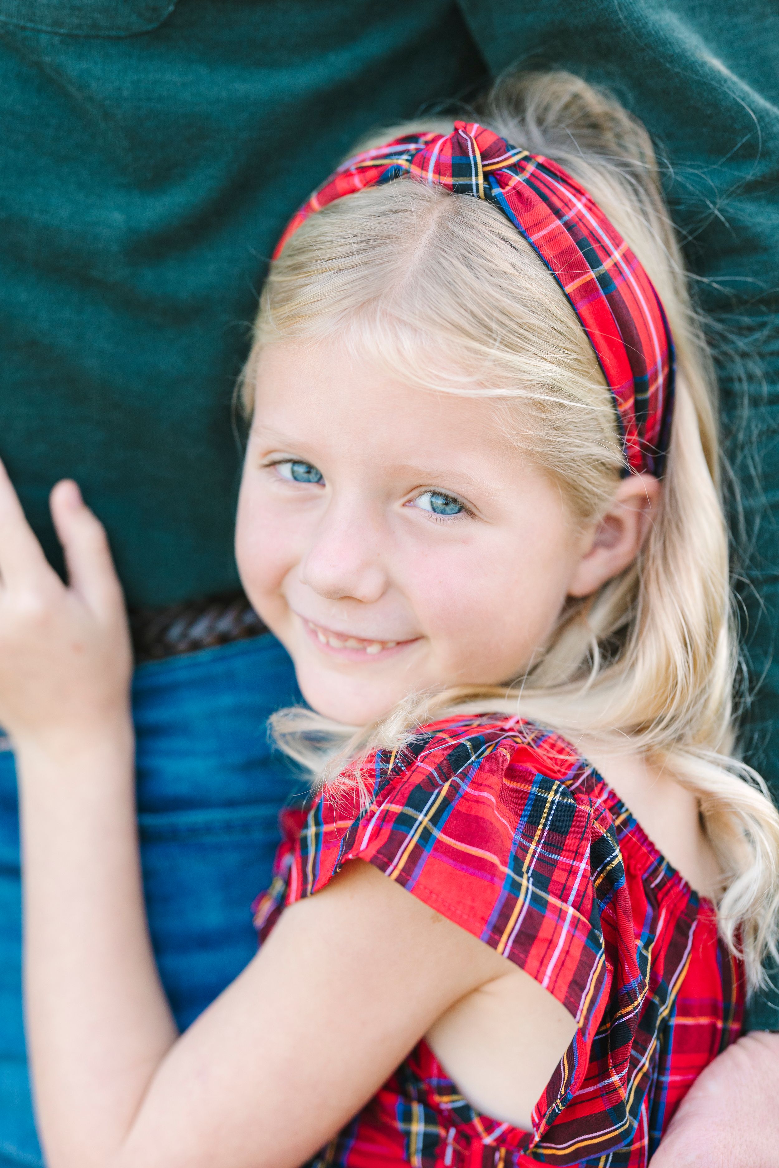 Young child in red plaid outfit smiling brightly against a dark blue background.
