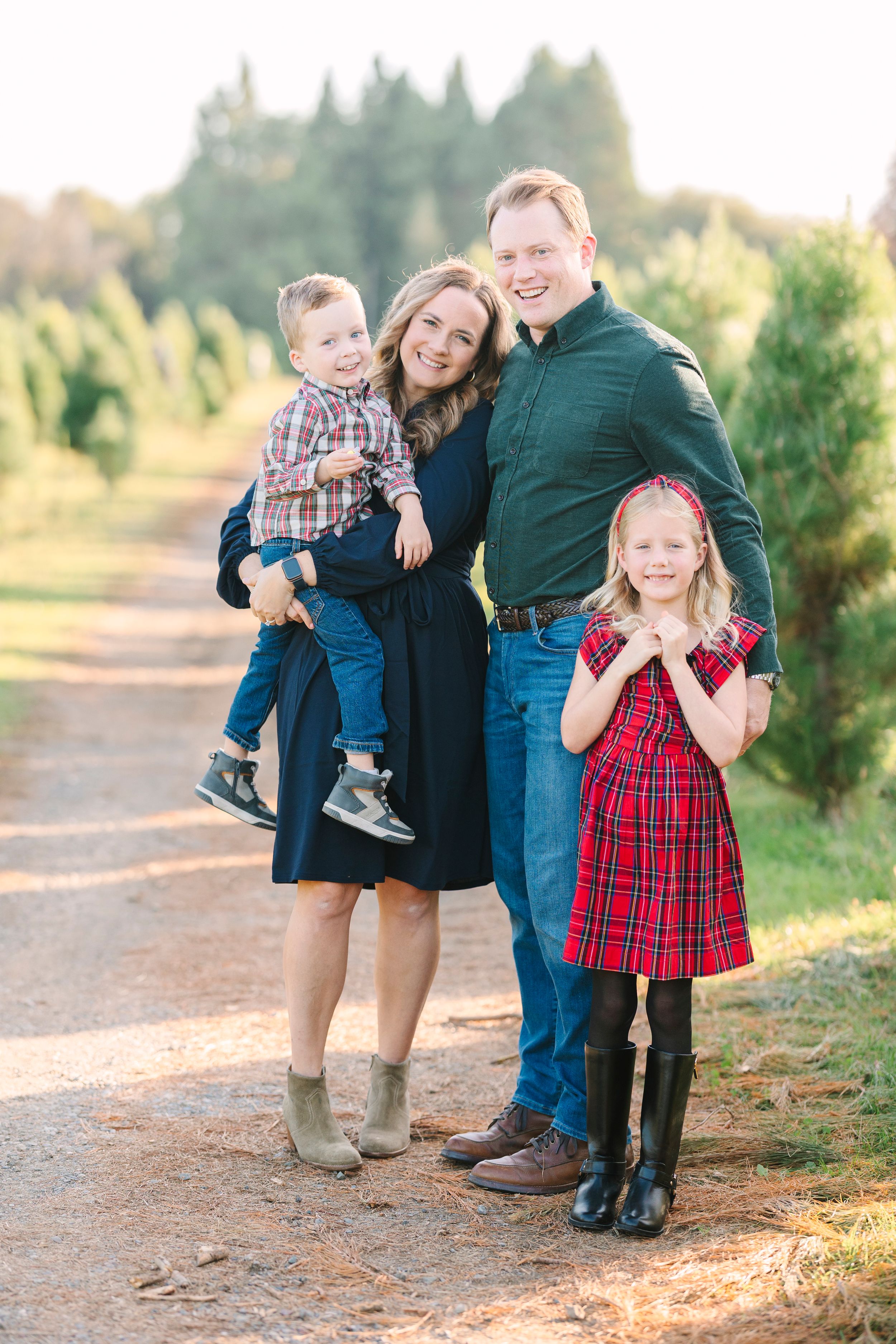 Family members share joyful moments together at a Christmas tree farm in coordinated outfits.