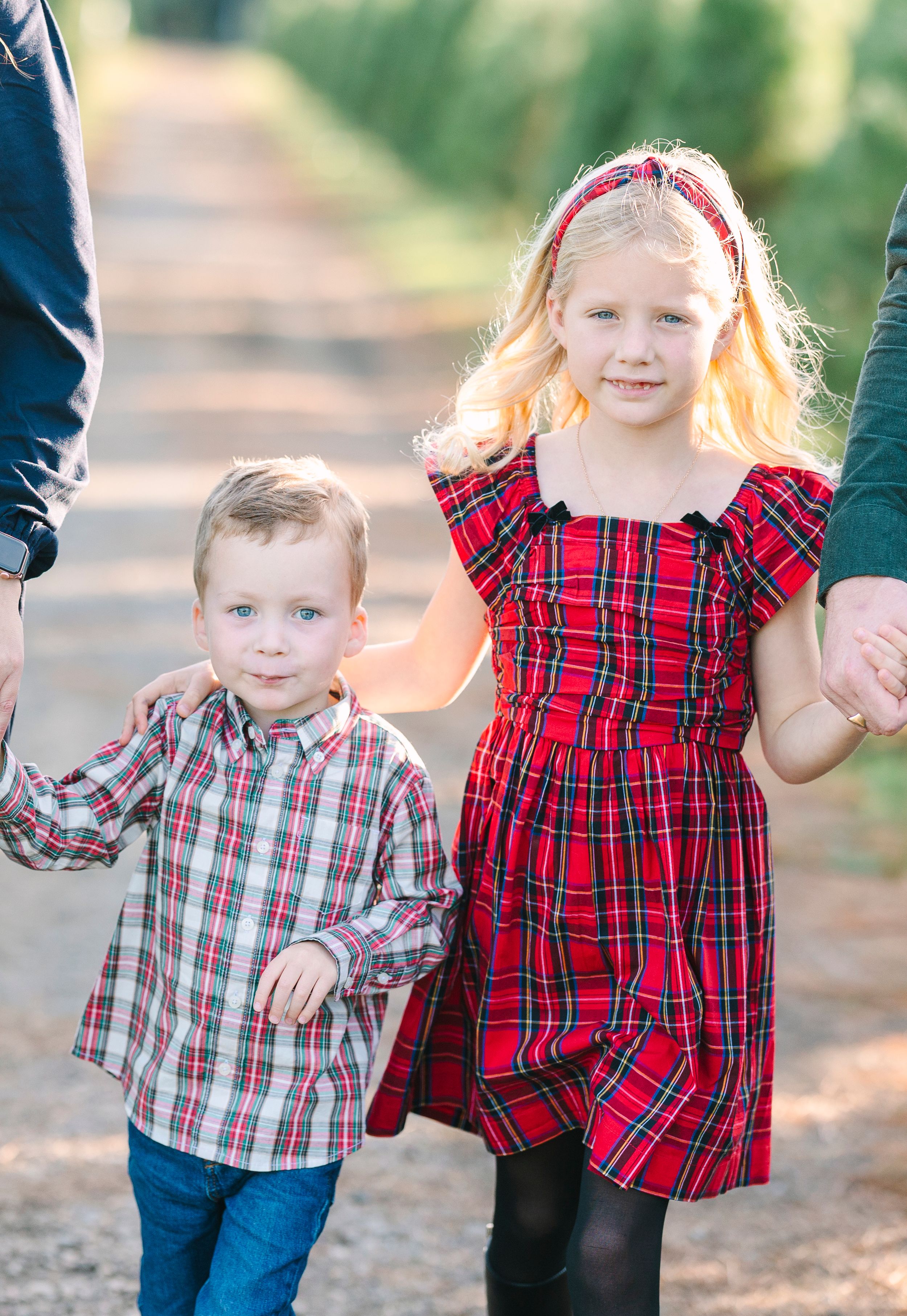 Two children wearing plaid shirts hold hands while walking outdoors.