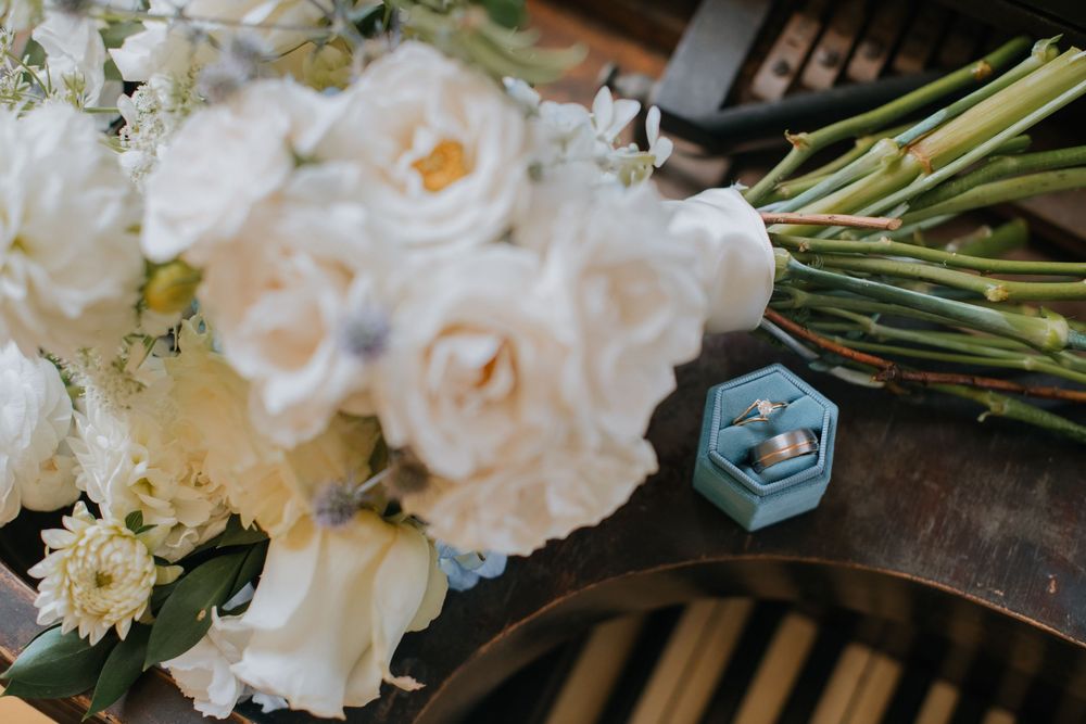 A delicate white floral arrangement with narcissus blooms and greenery stems on a dark wooden surface.