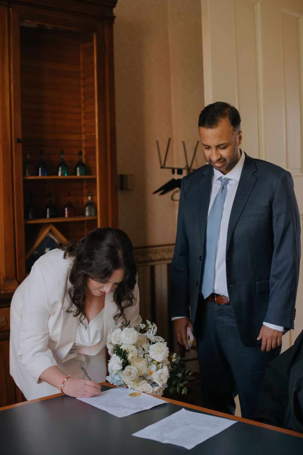 A sequence of photos showing a couple signing marriage documents in formal attire at an indoor venue.