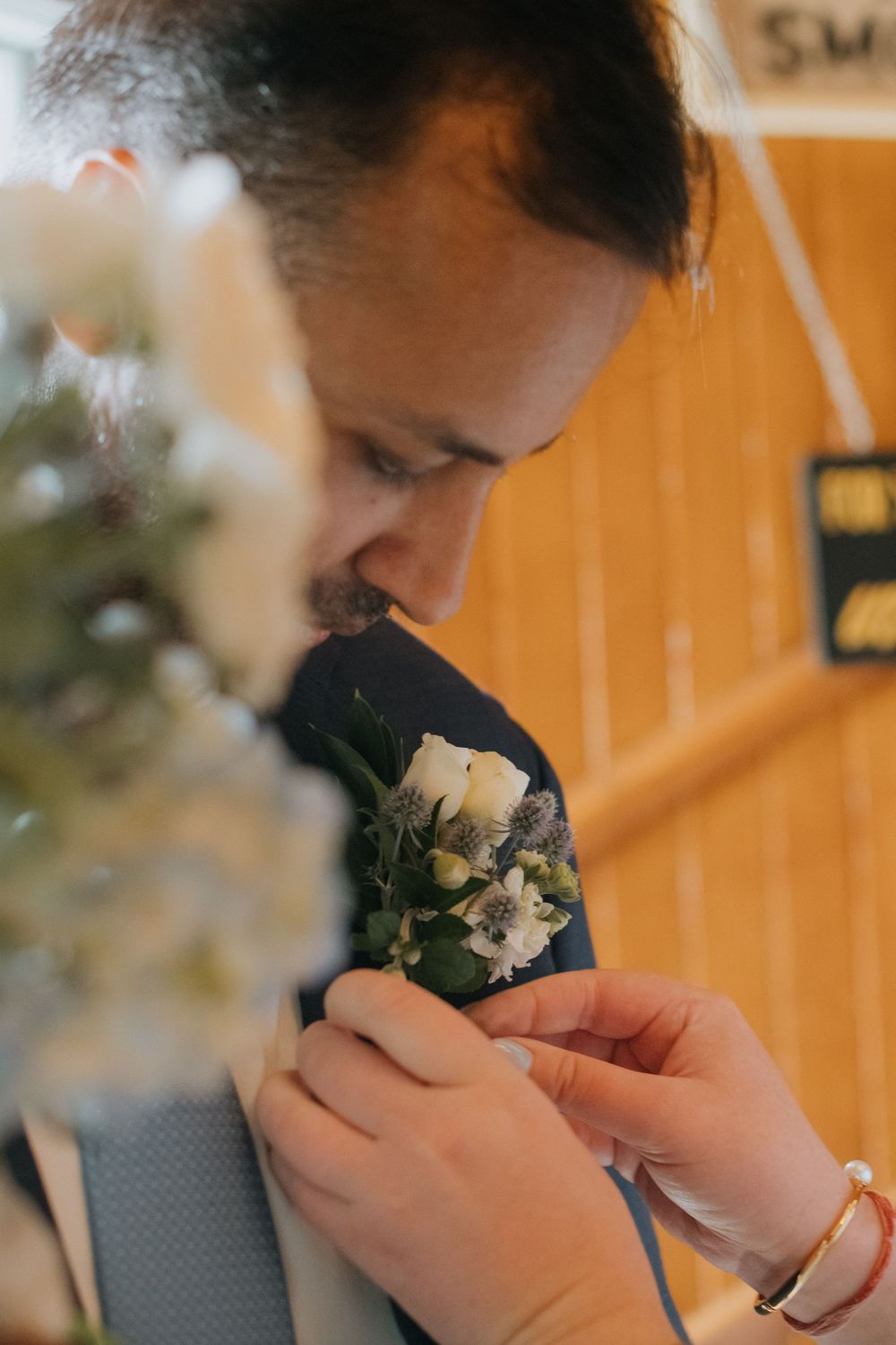 Person gently pinning white and green floral boutonniere to suit lapel in warm golden lighting.