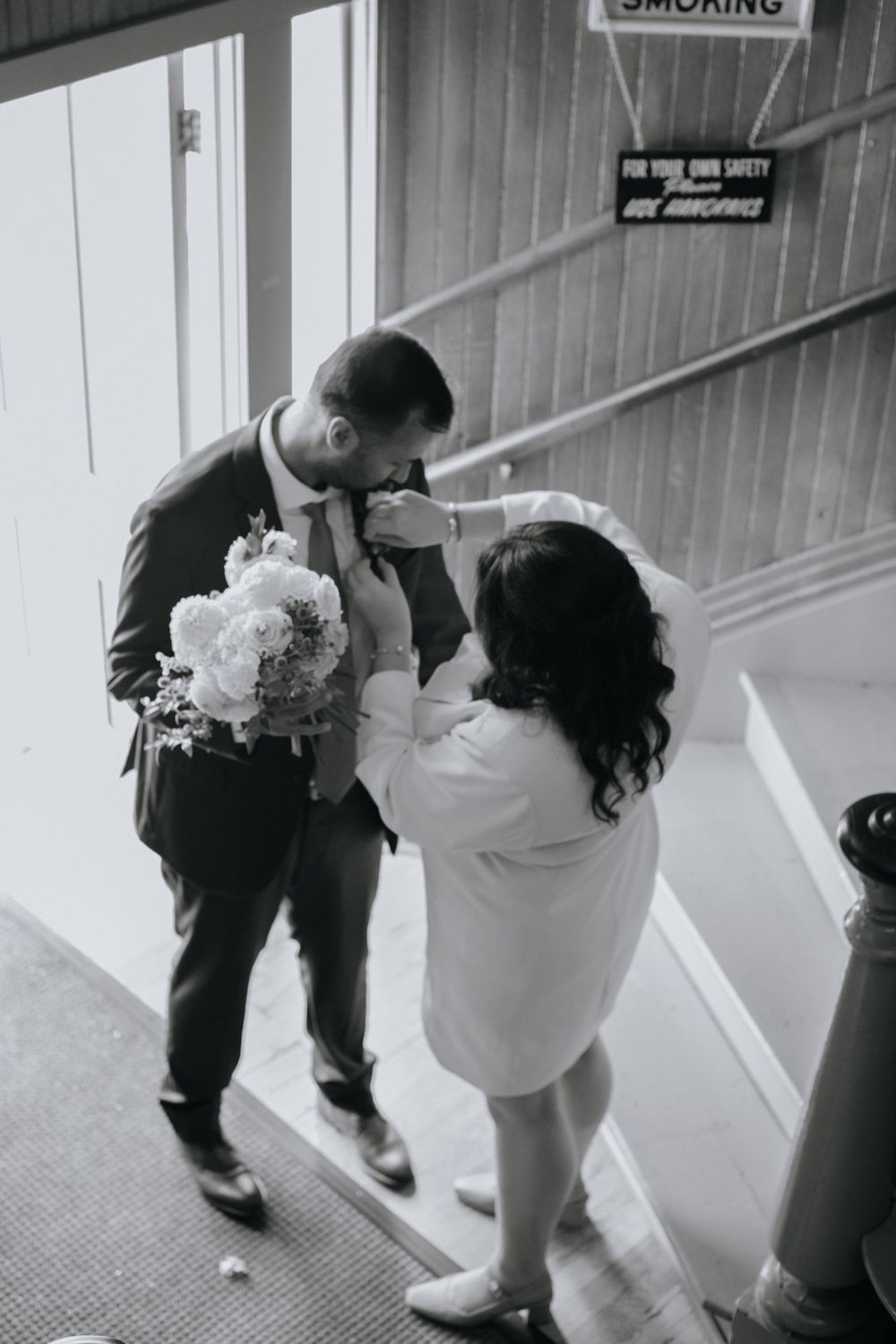 A wedding couple walking down a corridor as someone holds a white veil in black and white photography.