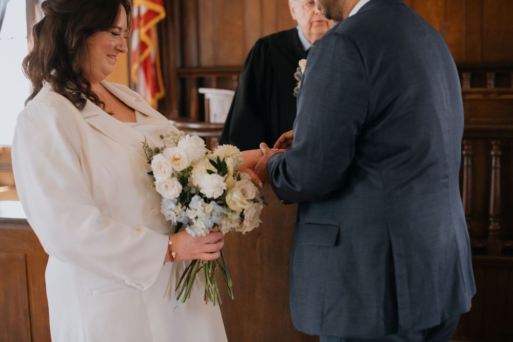 A couple shares a tender moment in formal attire while holding a bouquet of white flowers in a wood-paneled room.