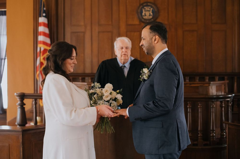 A couple shares an intimate moment during their wedding ceremony in a wood-paneled courthouse room.