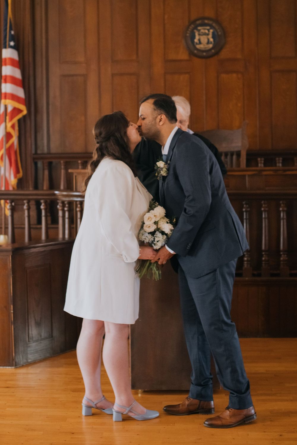 Romantic first kiss in wood-paneled courthouse room with American flag, captured in three sequential photos.