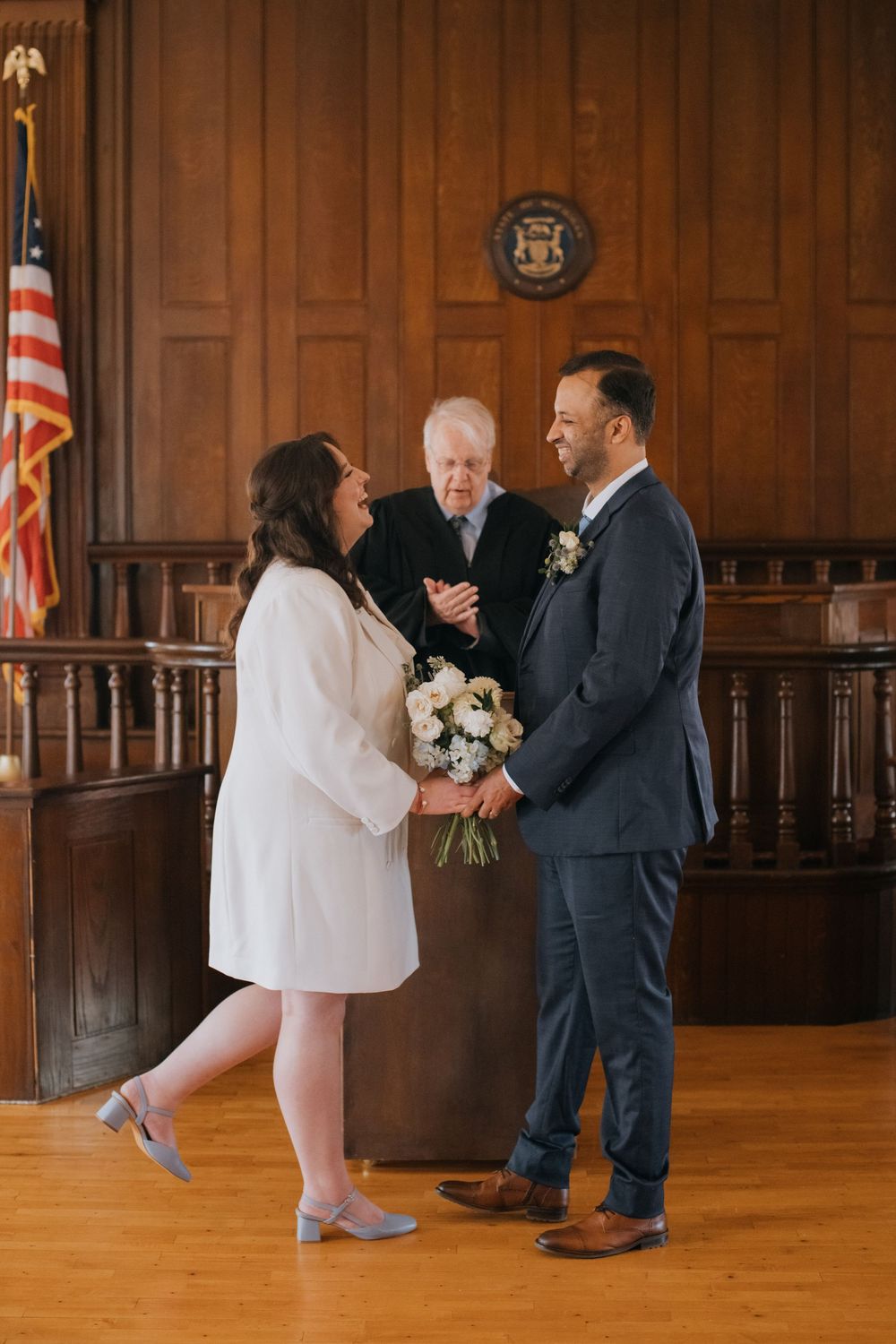 Couple sharing a joyful moment during their wedding ceremony in a wood-paneled room with an American flag.