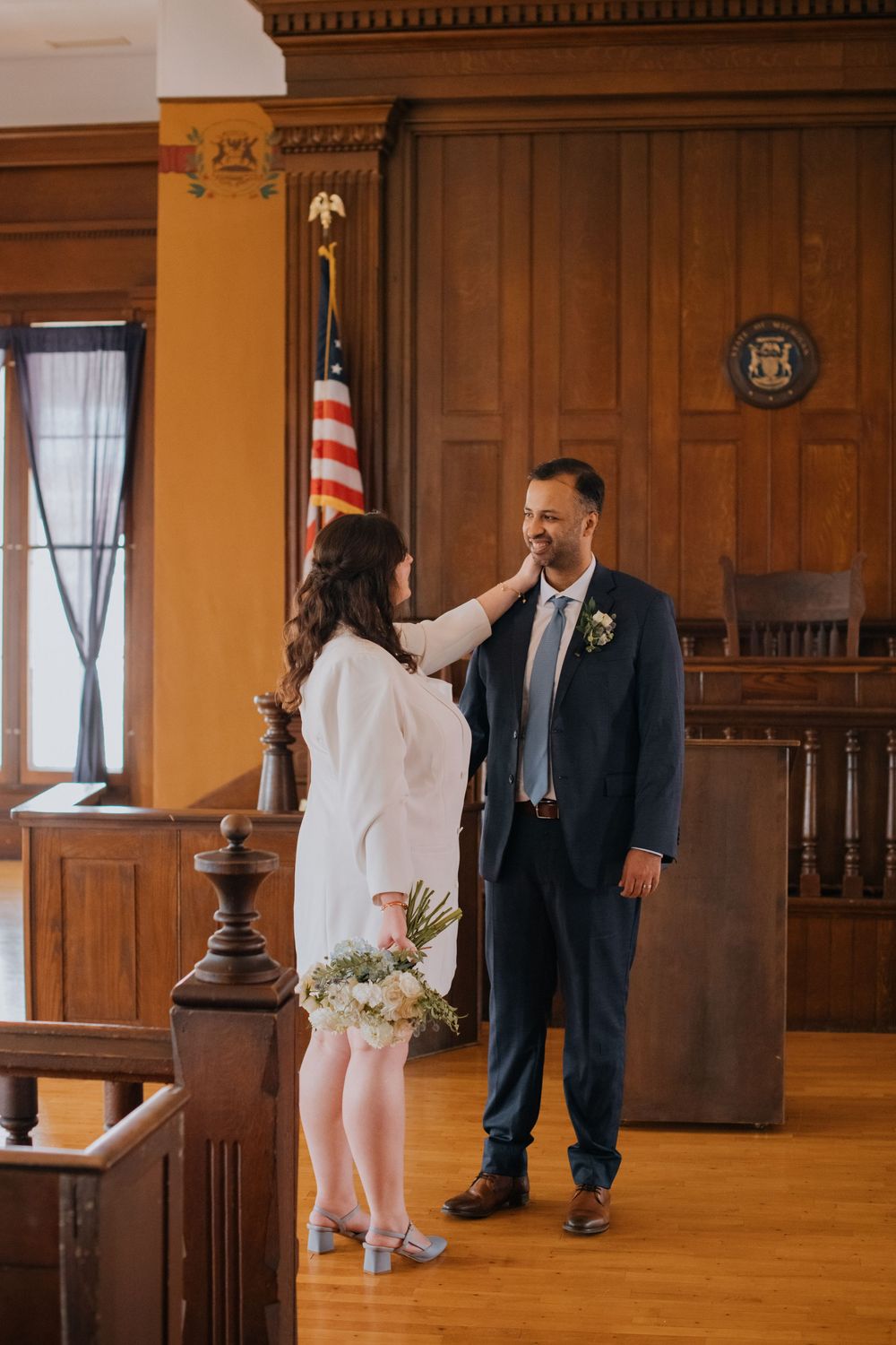 Couple sharing a playful moment in an elegant wood-paneled hallway with hardwood floors.