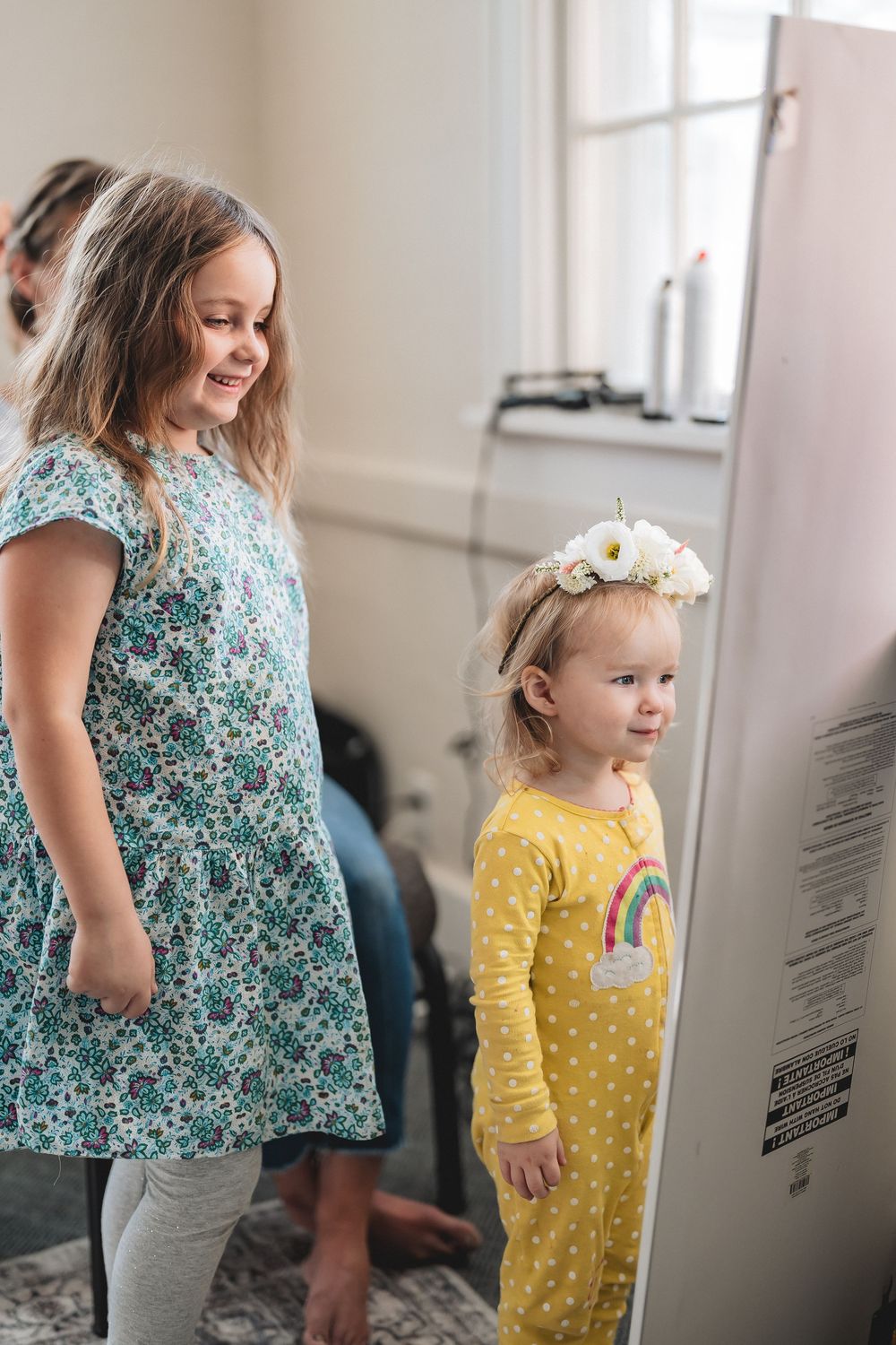A figure in a blue floral dress stands beside a smaller figure in a yellow polka dot outfit looking at wall text.