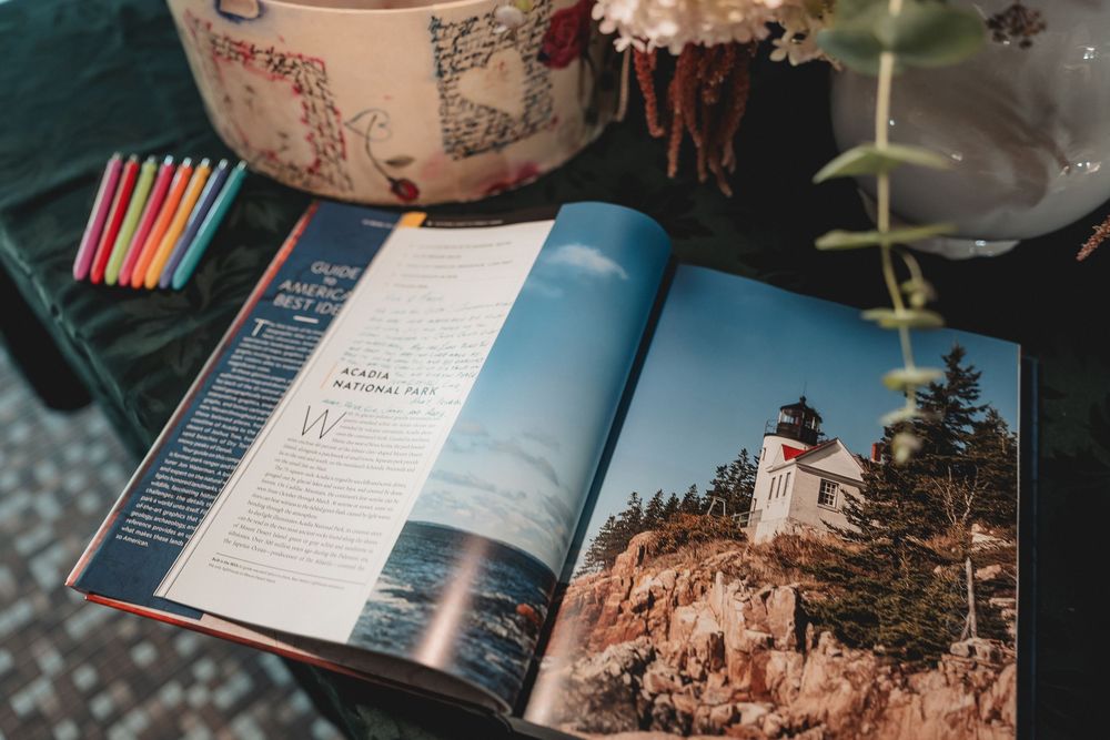 An open travel magazine showing a coastal lighthouse on a cliff beside colorful decorative elements.
