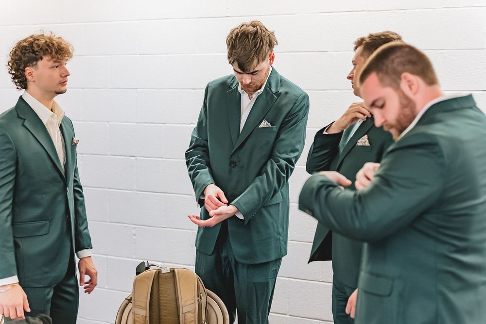 Groomsmen in dark green suits prepare together before wedding ceremony.