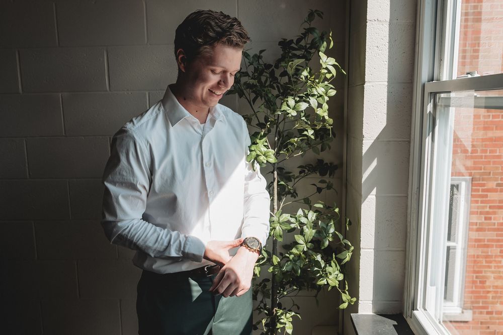 Person in white shirt stands by sunny window with plants, creating a bright and airy indoor scene.