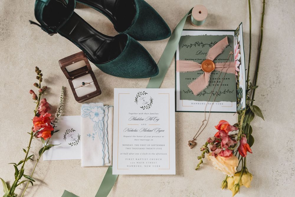 Wedding stationery and floral elements laid flat on white surface with green wedding shoes and colorful flowers.