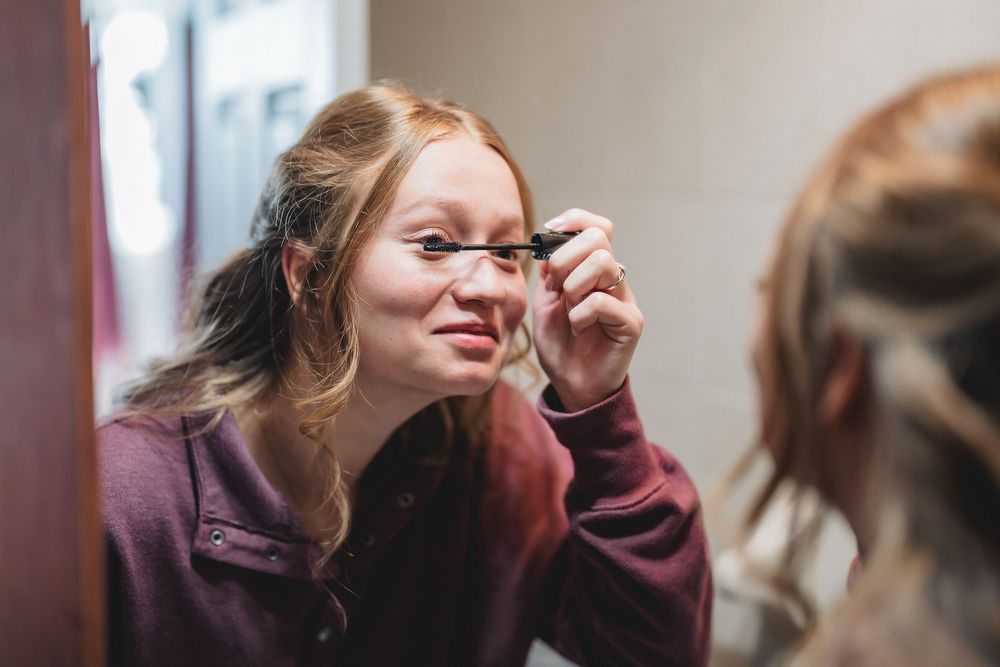Woman in a red sweater adjusts her glasses with a playful expression while having a conversation.