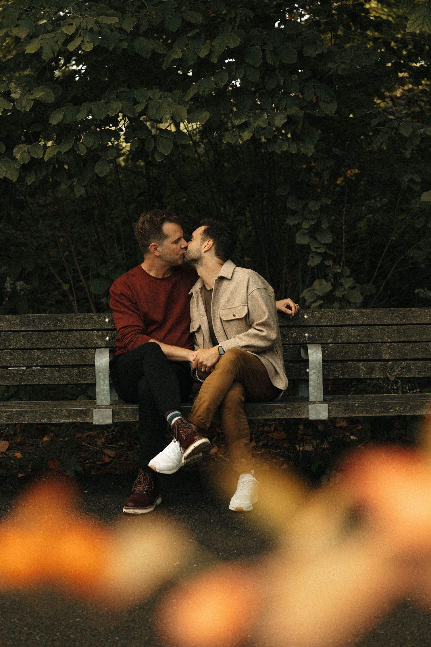 A romantic moment shared on a wooden bench surrounded by autumn foliage.