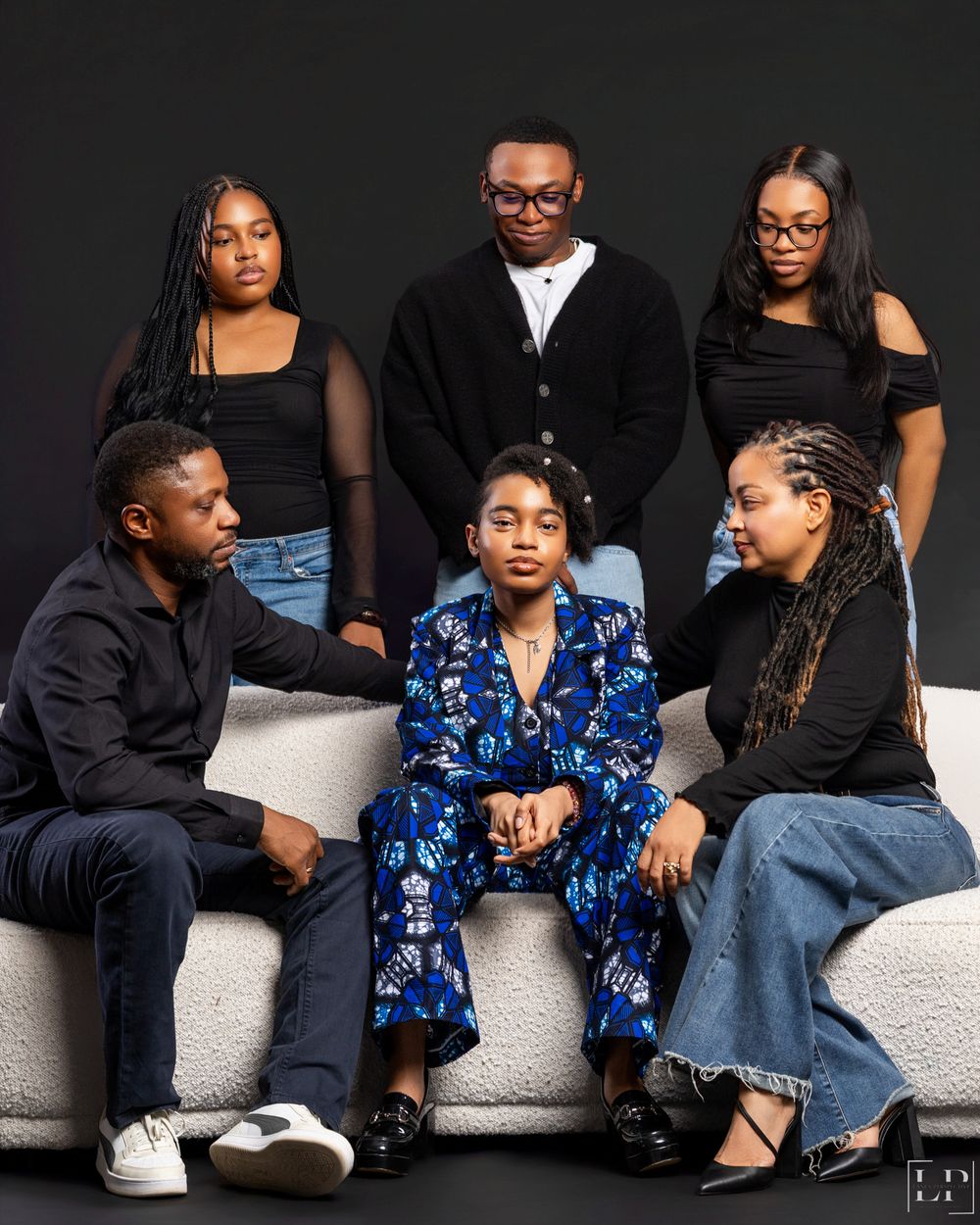 A group lounges casually on a white couch against a dark background wearing casual outfits and denim.