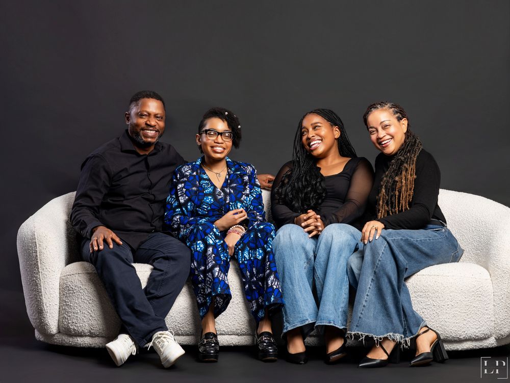 Casual group portrait of people lounging on white furniture against a dark background.