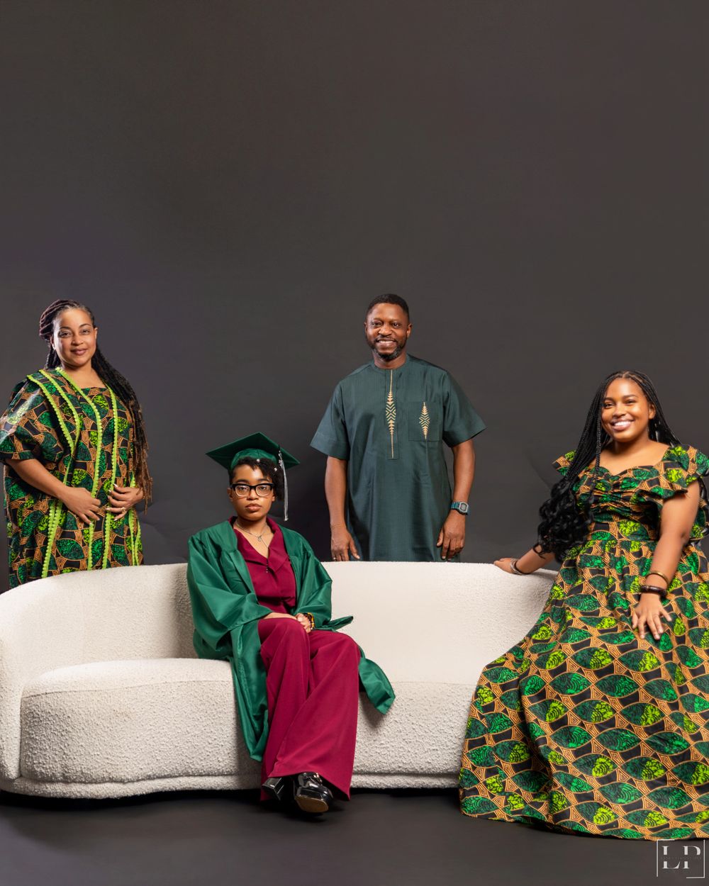 Group portrait on white couch featuring vibrant green and African print dresses with dark background.