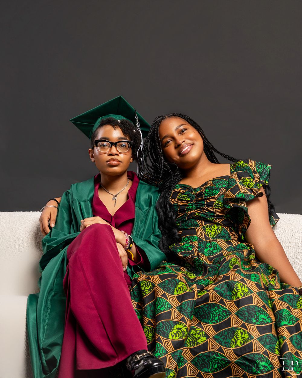 Close-up shot of people wearing green and burgundy outfits with African print dress on white couch.