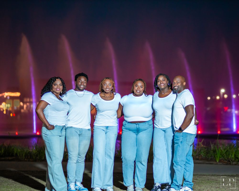 Group portrait with matching white shirts and light blue pants against evening city lights.