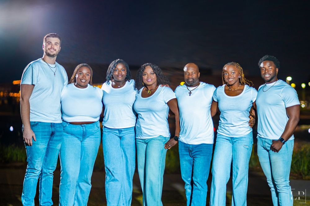 Wide group shot showing people in coordinated white and light blue outfits at night.