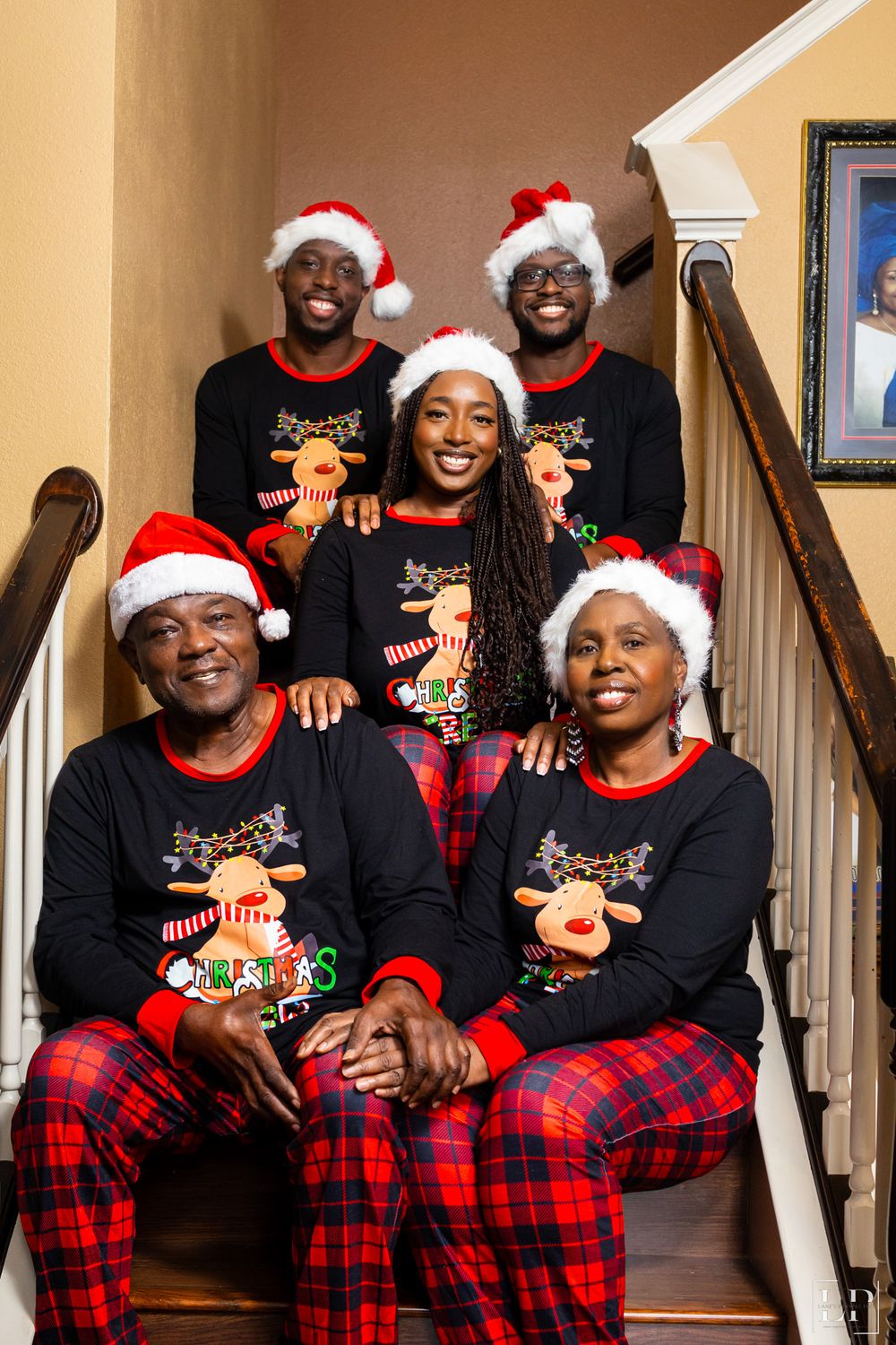 Holiday family photo on stairs wearing matching Christmas pajamas with Santa hats and reindeer sweaters.