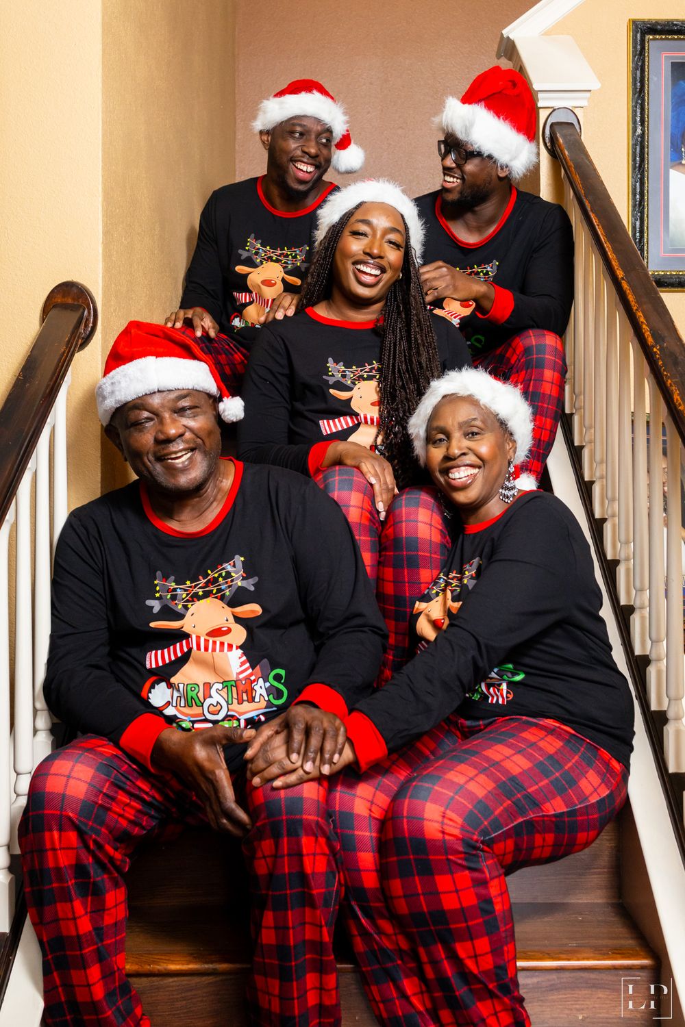 Group in matching red plaid pajamas and Santa hats pose playfully on wooden staircase.