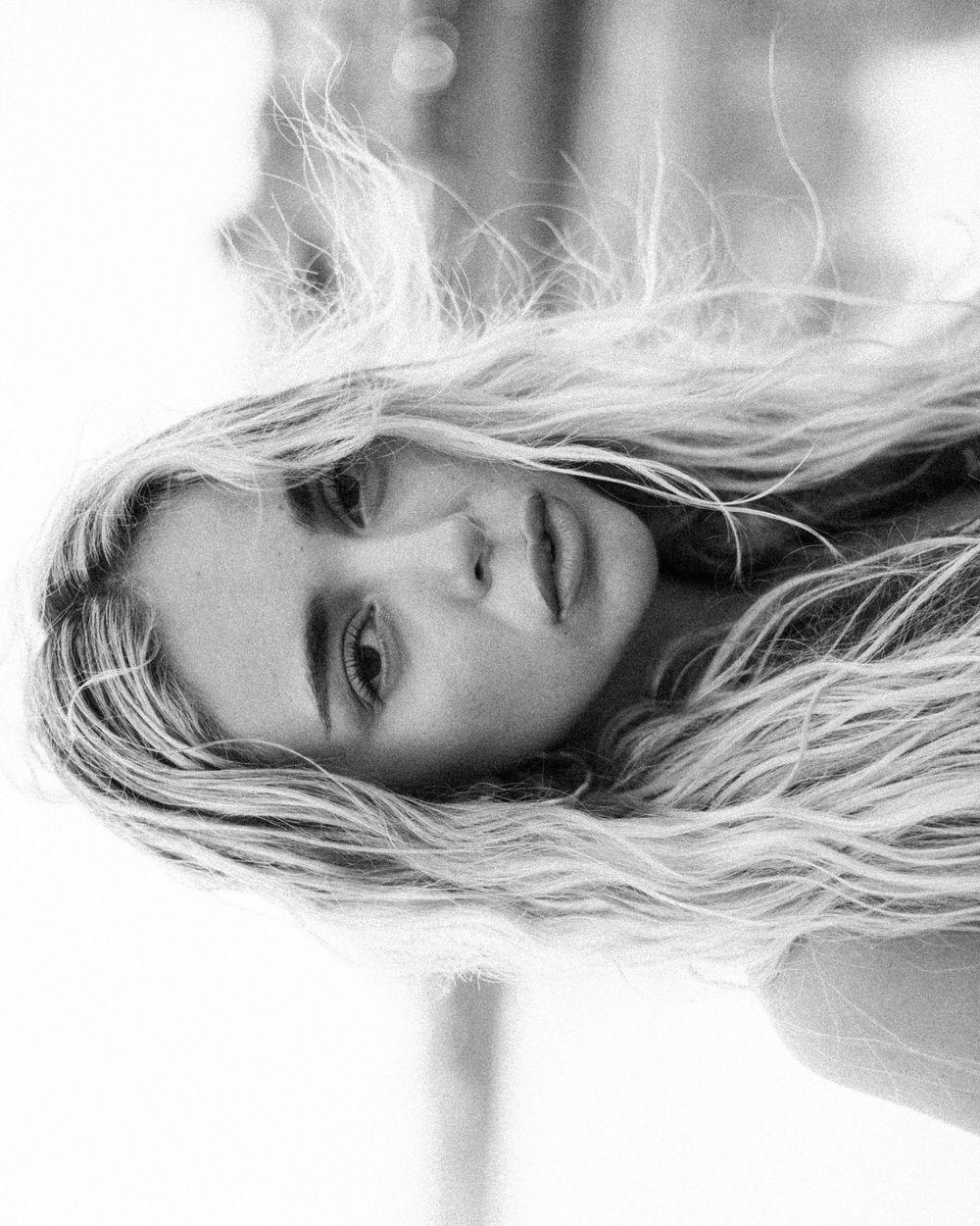 Artistic black and white close-up portrait with flowing blonde hair and dramatic side lighting.