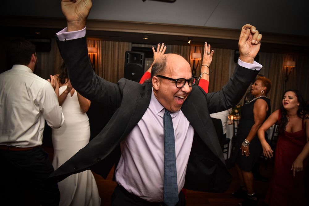 Wedding guests dancing and celebrating together on the dance floor at an indoor reception party.